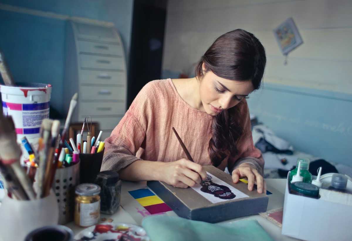 Woman painting a cat figure on a piece of paper.