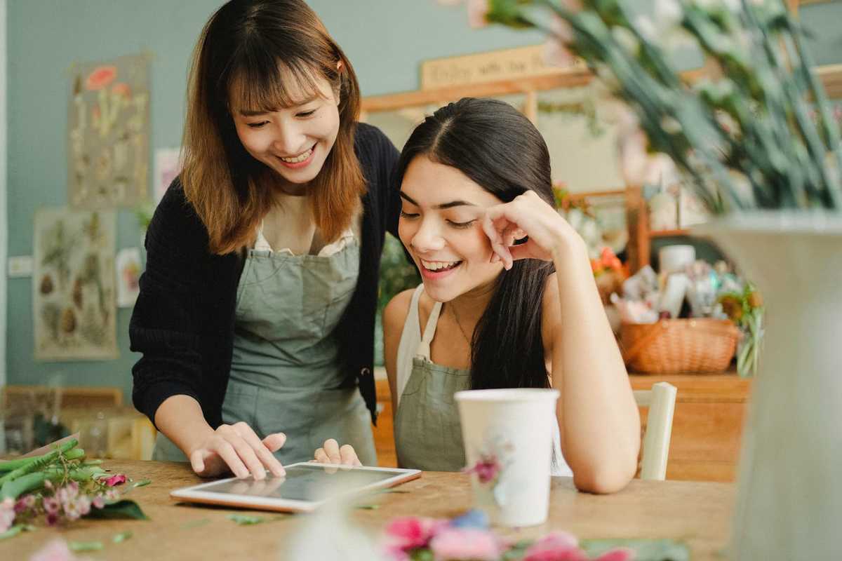 Two employees of a flower store look at the tablet on the table in front of them.