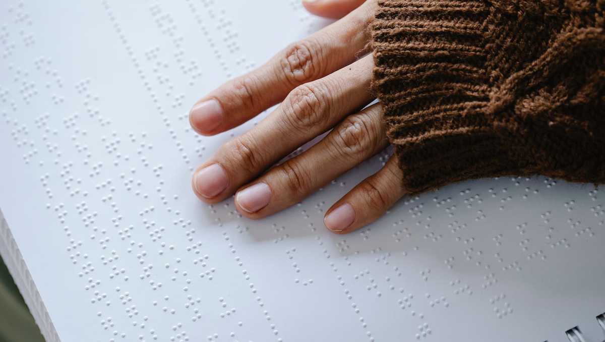 Finger berühren die Seite eines Buches in Braille-Schrift.