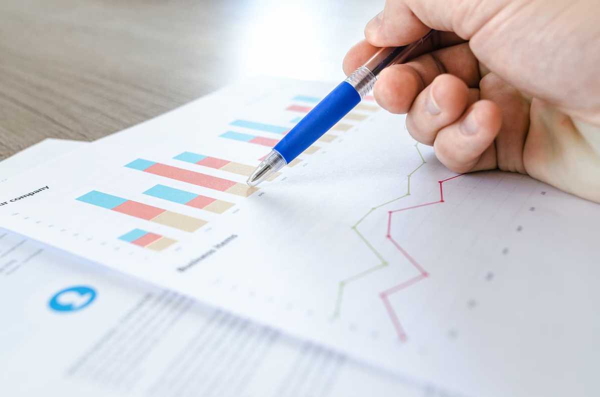 A ballpen pointing at column and line charts printed on a piece of paper.