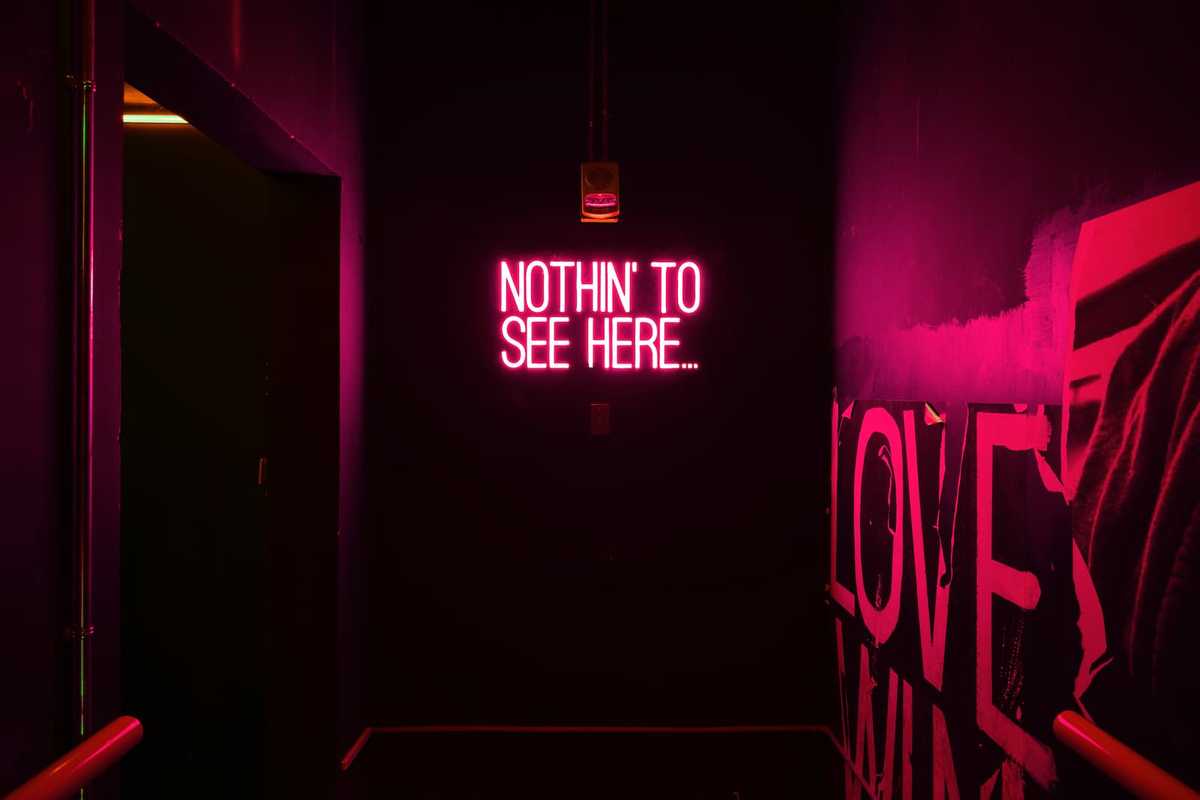 Ein dunkler Raum mit Neonlicht-Schrift an der Wand. Der Text lautet: 'Nichts zu sehen hier'.