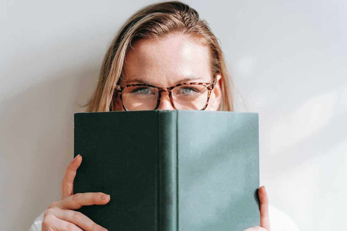 A woman's face partially hidden behind a book with a green cover.