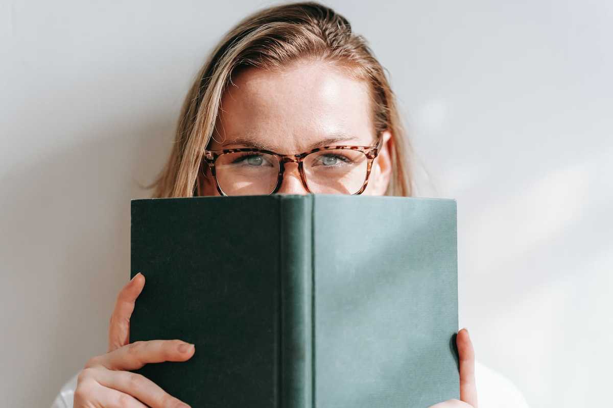 Das Gesicht einer Frau, das zur Hälfte von einem Buch mit grünem Umschlag verdeckt wird.